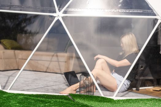 middle aged woman uses a laptop resting and spending time at Glamping house on holidays. holiday dome tent. Cozy, camping, hygge, lifestyle concept.