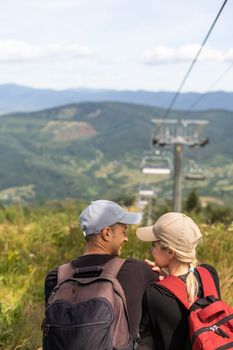 People sit on the ski elevator. View from the back. Summer, green forest. summer family vacation in the mountains