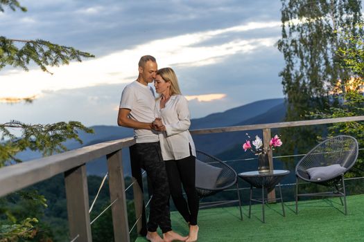 Horizontal sideview shot of a young couple in summer outfit enjoying the mountain view from terrace. Copy space