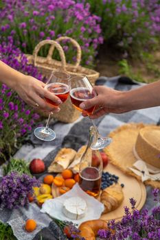 A man and a girl are holding glasses of wine on the background of a picnic in a lavender field. Selective focus