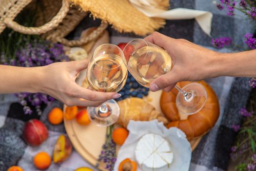A man and a girl are holding glasses of wine on the background of a picnic in a lavender field. Selective focus