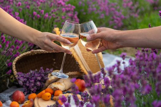 A man and a girl are holding glasses of wine on the background of a picnic in a lavender field. Selective focus