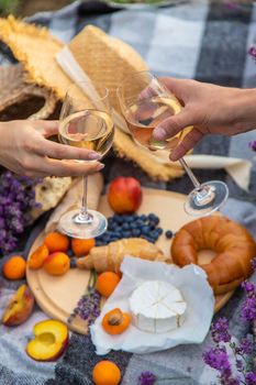 A man and a girl are holding glasses of wine on the background of a picnic in a lavender field. Selective focus