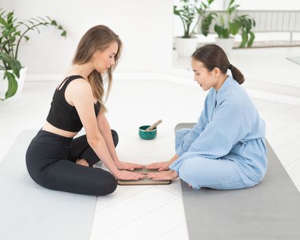 Two women sit on yoga mats with their hands on sadhu boards