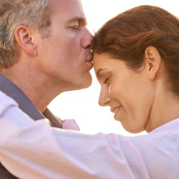 The love of my life. A mature man kissing his lovers forehead against a bright sky