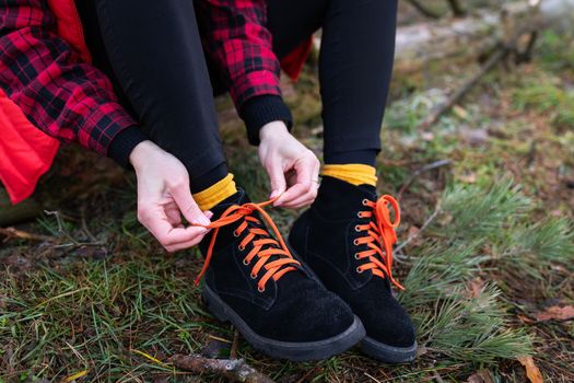 The girl is sitting on a log in the forest and tying bright shoelaces. Travel, trekking and hiking concept