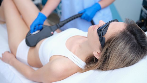 Laser hair removal and cosmetology in a beauty salon. Procedure for removing hair on abdomen of woman