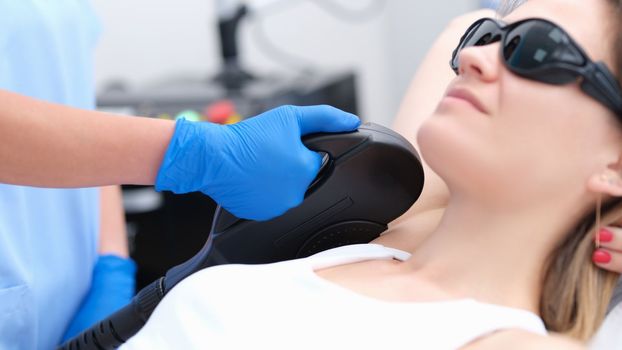Beautician makes laser hair removal procedure in armpit area of young woman in clinic. Hair removal procedure with photoepilator or laser hair removal of armpits in salon