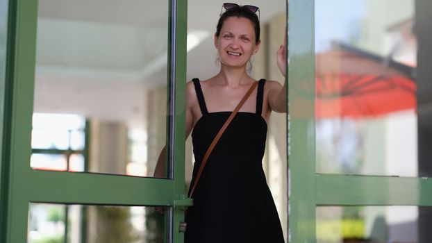Smiling happy emotionally joyful young woman opens doors. Meeting guests at door