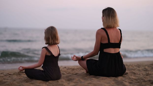 Woman with daughter on beach is doing yoga. Family relaxing yoga concept