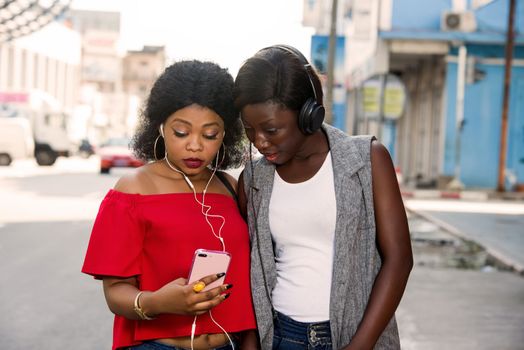 Two beautiful and happy young women are smiling, talking and looking for something on a cell phone in the city