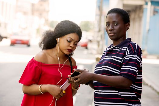 young girl standing in tee shirt showing her friend a mobile phone while looking at the camera.
