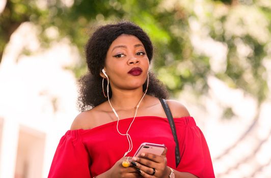 Happy young woman wearing a red t-shirt with headphones talking on the mobile phone in the city