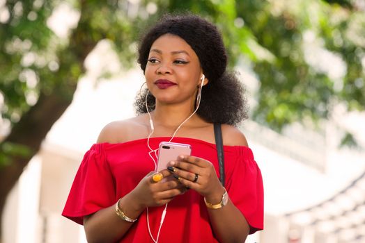 Happy young woman wearing a red t-shirt with headphones talking on the mobile phone in the city