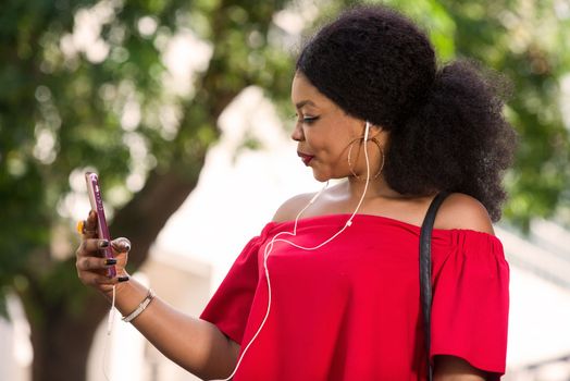 Happy young woman wearing a red t-shirt with headphones talking on the mobile phone in the city