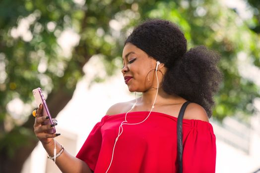Happy young woman wearing a red t-shirt with headphones talking on the mobile phone in the city