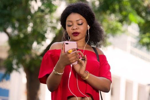 Happy young woman wearing a red t-shirt with headphones talking on the mobile phone in the city