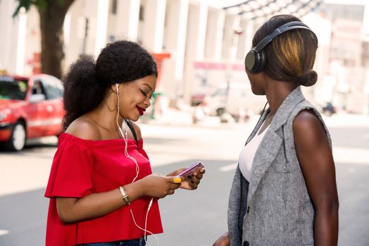 group of two happy smiling friends with headphones listening to music outdoors.persons, friendship and international concept