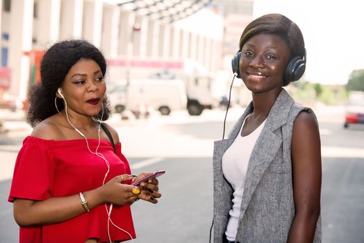 group of two happy smiling friends with headphones listening to music outdoors.persons, friendship and international concept