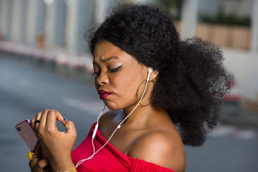 Pretty fashionable young woman talking on the phone checking her nail polish outdoors on a street