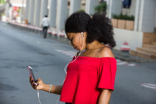 Portrait of beautiful girl with long hair and holding smart phone and wearing headphones laughing at the funny video she is looking at online. Technology concept