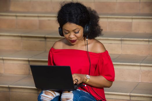 young girl sitting with laptop listening to music using headphones.