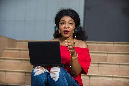 young girl sitting with laptop listening to music using headphones while smiling.