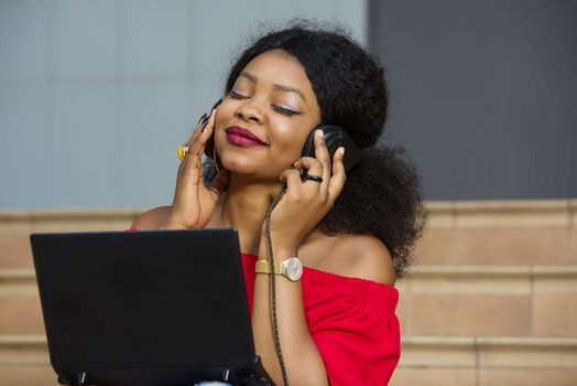 young girl sitting with laptop listening to music using headphones and looking at the camera smiling.