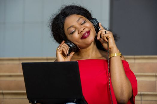 young girl sitting with laptop listening to music using headphones while smiling