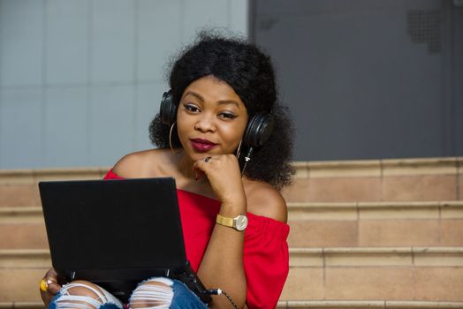 young girl sitting with laptop listening to music using headphones and looking at the camera smiling.