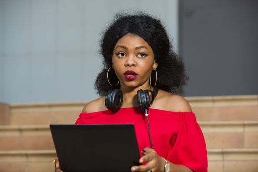 young girl sitting with laptop watching the camera headphones on the neck.