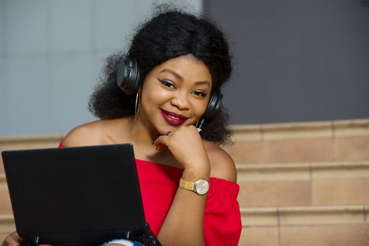 young girl sitting with laptop listening to music using headphones and looking at the camera smiling .