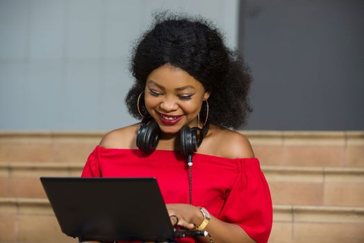young girl sitting with headphones in the neck looking at laptop laughing.