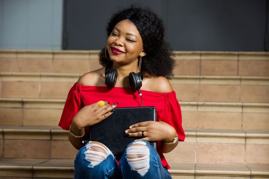 young girl sitting on stairs in red camisole with computer watching the camera smiling.