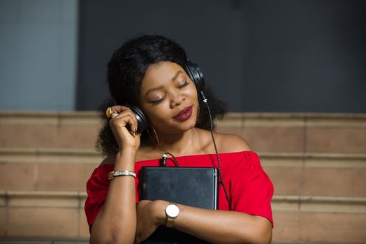 young girl sitting in red camisole with laptop listening to music using headphones closed eyes smiling.