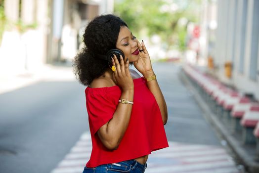 Young happy woman wearing casual clothes with afro hairstyle is standing in town on a street talking on the phone