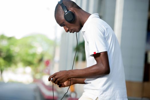 people, music, technology, leisure and lifestyle - Happy african young man with headphones and smart phone on the street