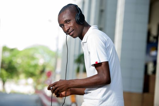 people, music, technology, leisure and lifestyle - Happy african young man with headphones and smart phone on the street