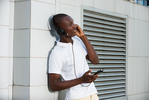people, music, technology, leisure and lifestyle - Happy african young man with headphones and smart phone on the street