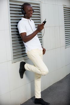 people, music, technology, leisure and lifestyle - Happy african young man with headphones and smart phone on the street