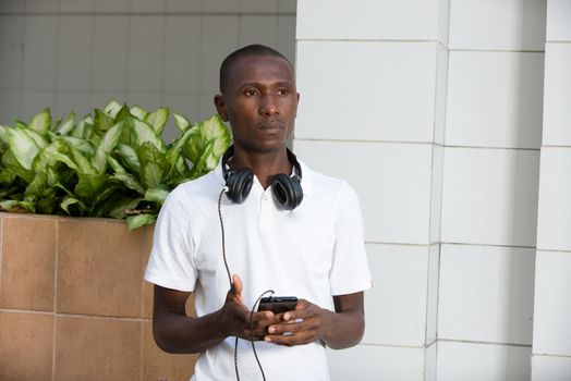 Young man with casual clothes standing thoughtful with headphones and smart phone on the street