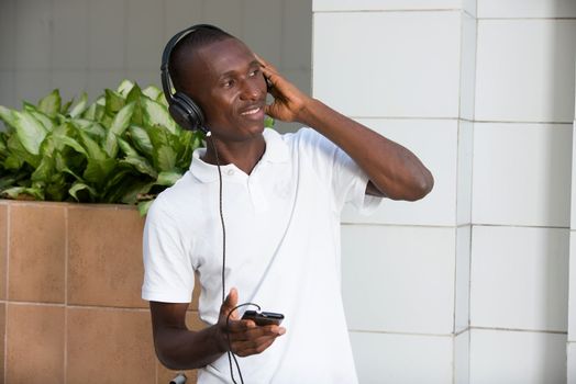 people, music, technology, leisure and lifestyle - Happy african young man with headphones and smart phone on the street