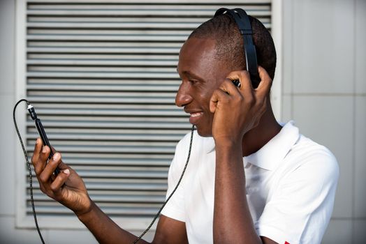 happy young man in white t-shirt listening to music with mobile phone headset and singing outdoors. Student with smart phone and headphones