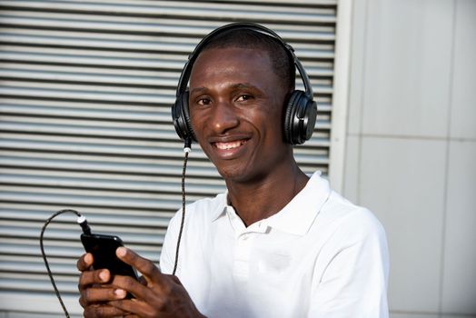 happy young man in white t-shirt listening to music with mobile phone headset and singing outdoors. Student with smart phone and headphones