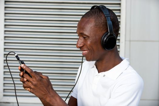 happy young man in white t-shirt listening to music with mobile phone headset and singing outdoors. Student with smart phone and headphones
