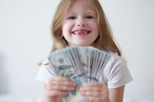 Portrait of happy smiling little girl with fan of dollars. Financial earnings in childhood concept