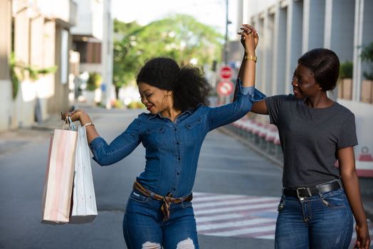 two happy friends carrying shopping bags walking and dancing in the city