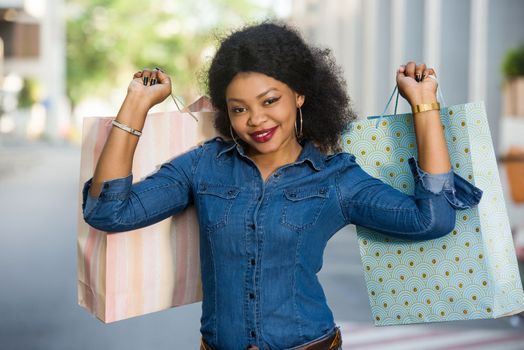 Young cheerful woman holding many colorful shopping bags in the city