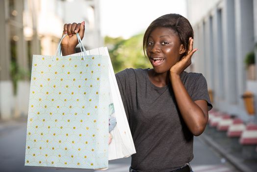 surprised woman to see something, holding shopping bags looks at the camera while listening hands on an ear