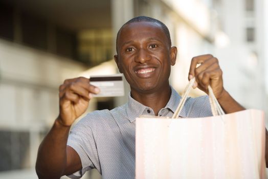 smiling man showing and holding shopping bags with credit card outdoors
